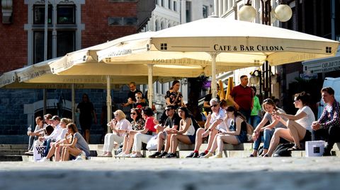 Zahlreiche Menschen sitzen in der Innenstadt von Oldenburg auf den Treppen am Rathausmarkt, wo sonst die Tische und Stühle der Gastronomie unter Schirmen stehen