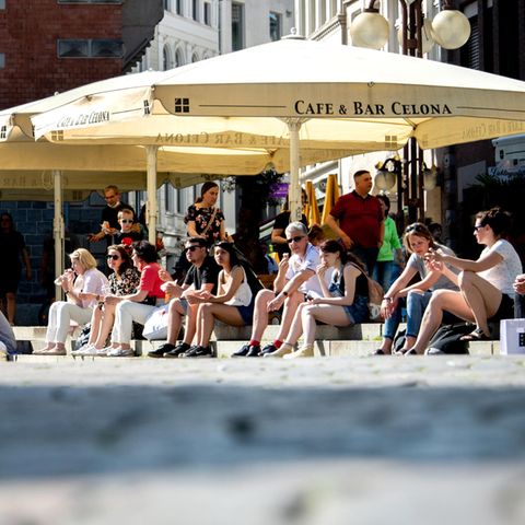 Zahlreiche Menschen sitzen in der Innenstadt von Oldenburg auf den Treppen am Rathausmarkt, wo sonst die Tische und Stühle der Gastronomie unter Schirmen stehen