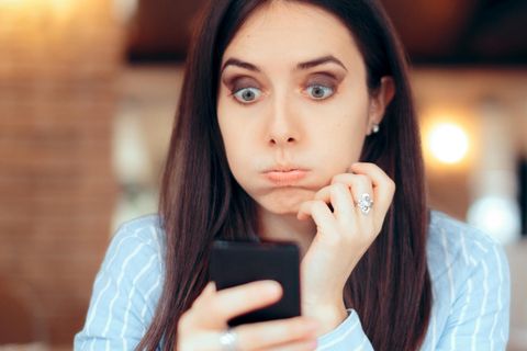 Frau schaut genervt auf ihr Smartphone