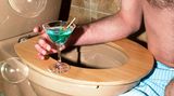Ein Cocktailglas steht auf einer Toilettenbrille