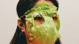 Eine Frau trägt ein Salatblatt mit Augenlöchern vor dem Gesicht