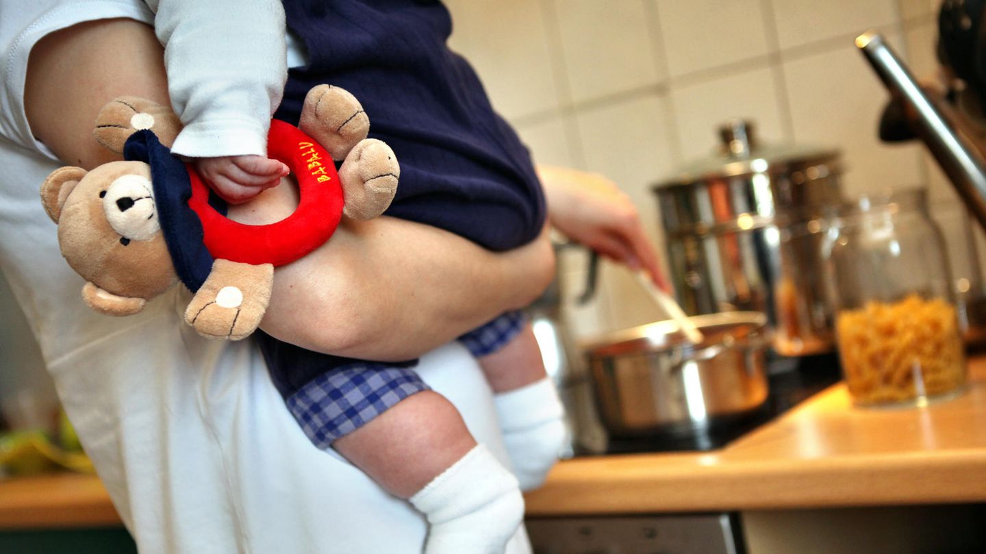 Eine Mutter hält beim Kochen ihr Kleinkind auf dem Arm