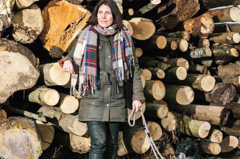 Hund und Besitzerin stehen vor einem Holzstapel