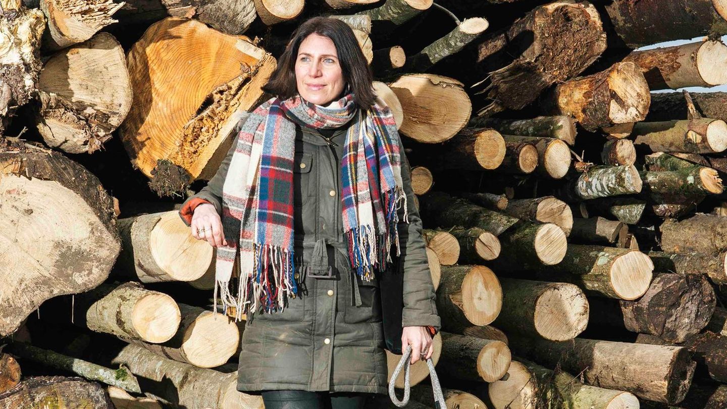 Hund und Besitzerin stehen vor einem Holzstapel