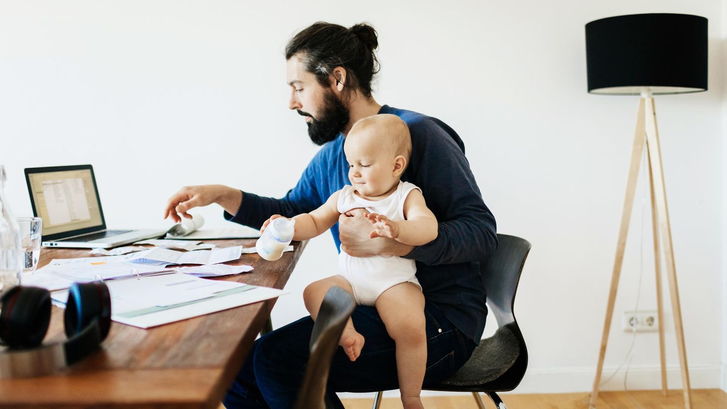 Mann sitzt vor Laptop mit Baby auf dem Schoß Mann sitzt vor Laptop mit Baby auf dem Schoß