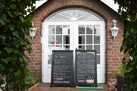 Vor der weißen Flügeltür in ein Backstein-Gebäude stehen zwei Tafeln, auf denen denen das Restaurant auf Corona-Fälle hinweist