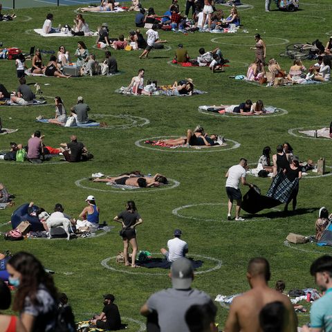 Besucher sitzen im Park in eingezeichneten Kreisen, die bei der Umsetzung der Abstandsregeln helfen sollen