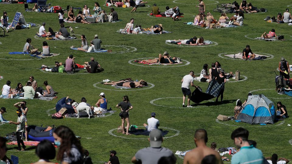 Besucher sitzen im Park in eingezeichneten Kreisen, die bei der Umsetzung der Abstandsregeln helfen sollen
