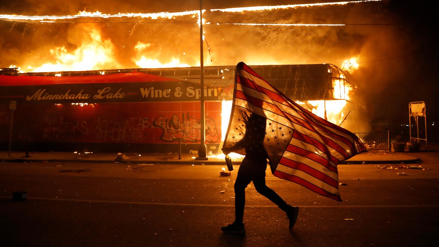 Mensch mit amerikanischer Flagge vor brennendem Geschäft Mensch mit amerikanischer Flagge vor brennendem Geschäft