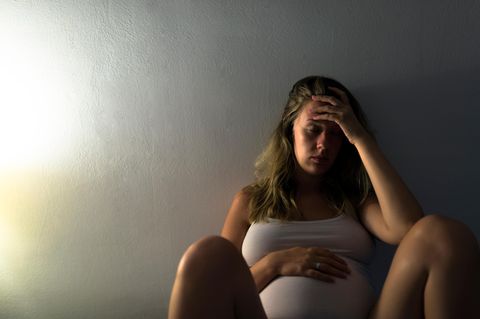 Schwangere Frau hält sich Bauch und Kopf
