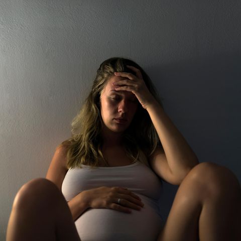 Schwangere Frau hält sich Bauch und Kopf