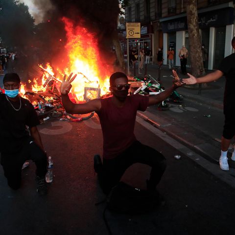 Frankreich, Paris: Demonstranten knien nieder und reagieren vor einer brennenden Barrikade.
