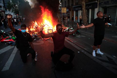 Frankreich, Paris: Demonstranten knien nieder und reagieren vor einer brennenden Barrikade.
