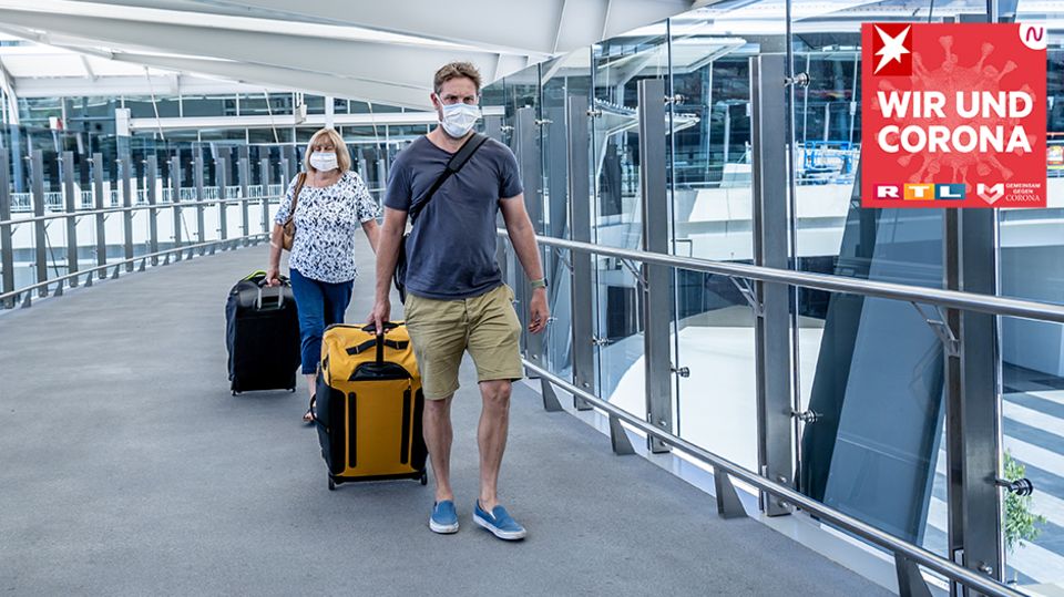 Wir und Corona: Reisende mit Koffer und Mundschutz