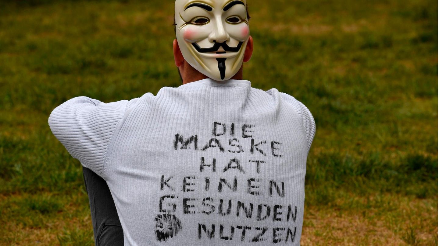 Ein junger Mann sitzt auf einer Wiese und hat "Die Maske hat keinen gesunden Nutzen" auf dem Rücken geschrieben