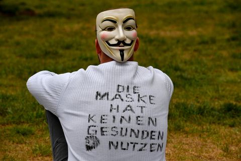 Ein junger Mann sitzt auf einer Wiese und hat "Die Maske hat keinen gesunden Nutzen" auf dem Rücken geschrieben