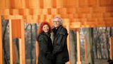 Das Paar steht lächelnd vor organgefarbenen Tüchern im Central Park in New York
