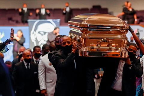 Männer in schwarzen Anzügen tragen einen goldglänzenden Sarg aus einer vollen Kirche