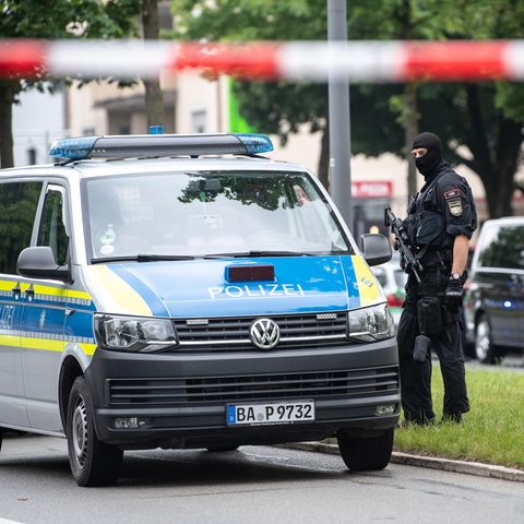 Neben einem VW-Bus der Polizei steht ein Polizist mit Maschinenpistole und Sturmhaube