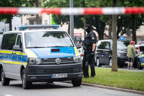 Neben einem VW-Bus der Polizei steht ein Polizist mit Maschinenpistole und Sturmhaube