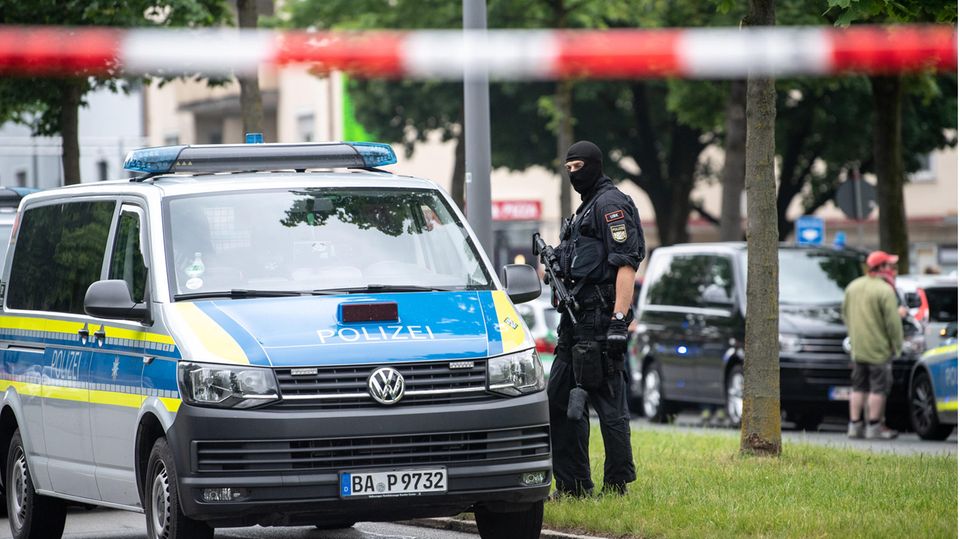 Neben einem VW-Bus der Polizei steht ein Polizist mit Maschinenpistole und Sturmhaube