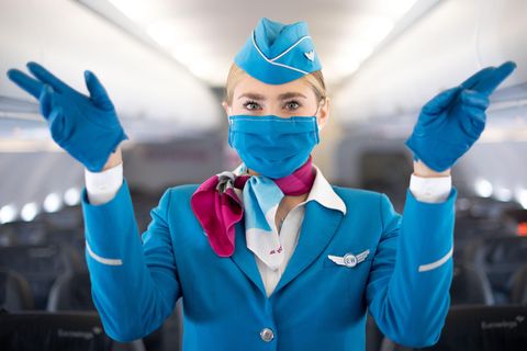 Sicherheitsanweisung mit Fingerzeig auf die Notausgänge: Diese Flugbegleiterin trägt einen Mund-Nasen-Schutz.