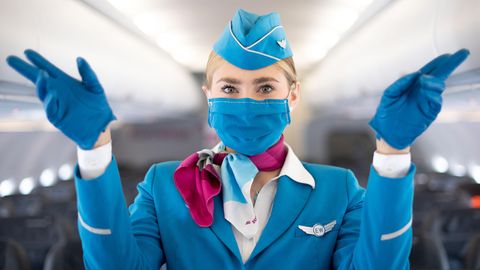 Sicherheitsanweisung mit Fingerzeig auf die Notausgänge: Diese Flugbegleiterin trägt einen Mund-Nasen-Schutz.