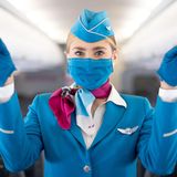 Sicherheitsanweisung mit Fingerzeig auf die Notausgänge: Diese Flugbegleiterin trägt einen Mund-Nasen-Schutz.