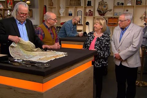 "Bares für Rares"-Experte Albert Maier nimmt die Stofflandkarten von Ehepaar Roth in Augenschein, Moderator Horst Lichter plaudert mit den Verkäufern.