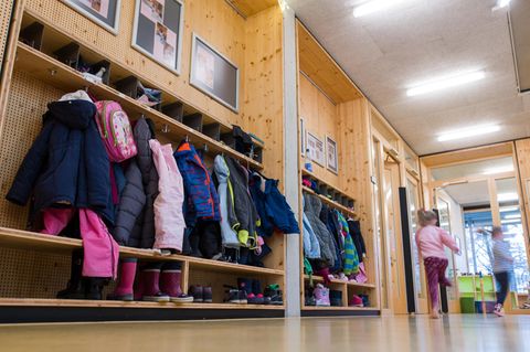 Zwei Mädchen laufen an einer Garderobe voller Kinderjacken vorbei