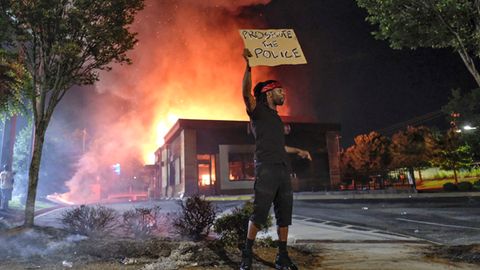  Ein Mann hält ein Schild, während im Hintergrund das Wendy's-Restaurant in Atlanta brennt.
