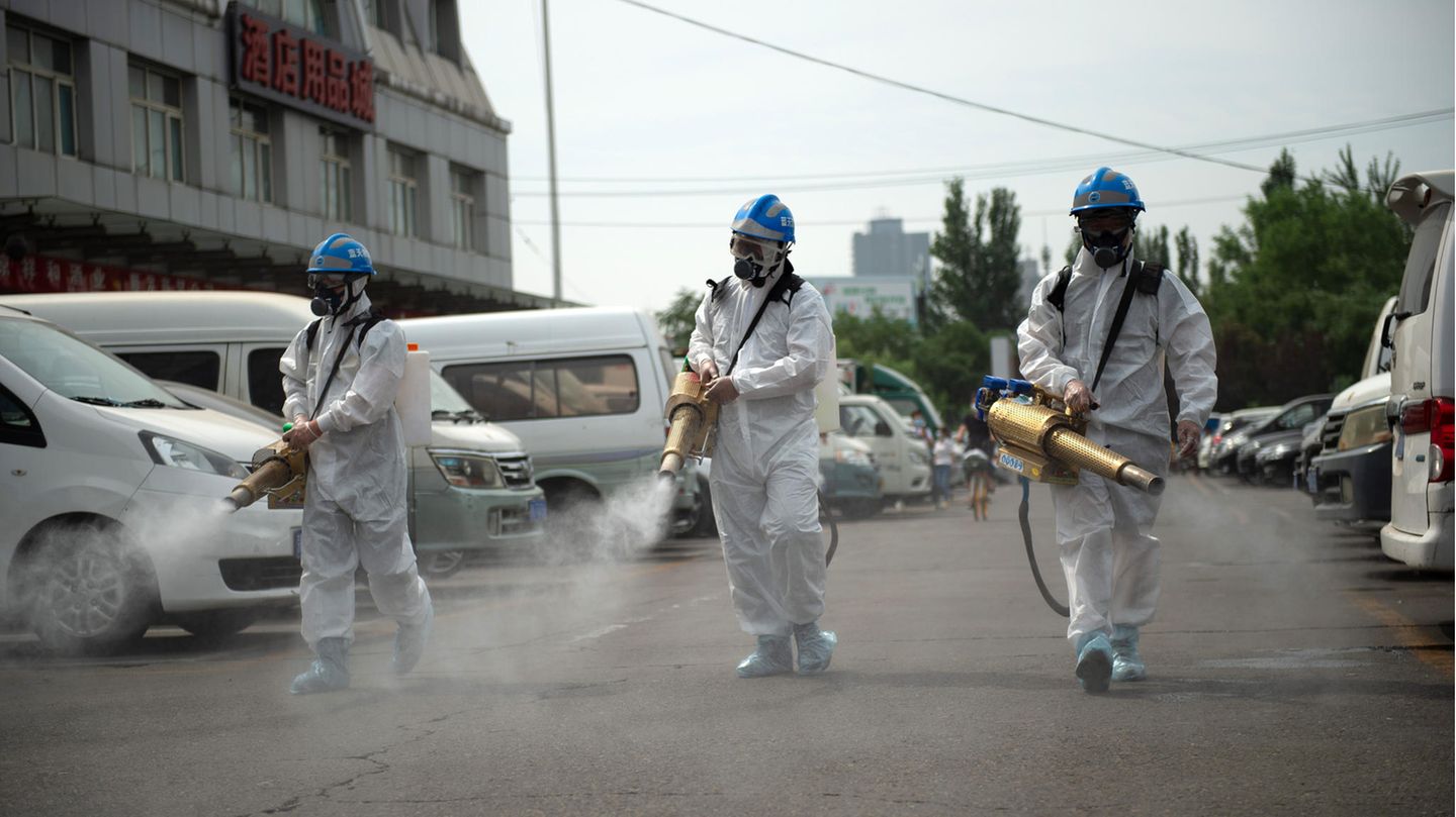 Morgenlage: In Schutzausrüstung säubern und desinfizieren drei Männer eine Straße in Peking