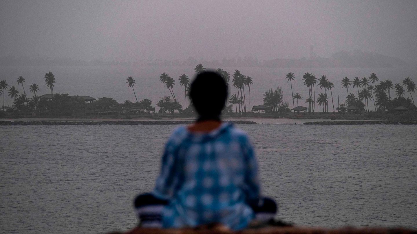 Eine Frau meditiert vor dem Panorama der Stadt San Juan, die von einer riesigen Wolke aus Saharastaub verhüllt ist