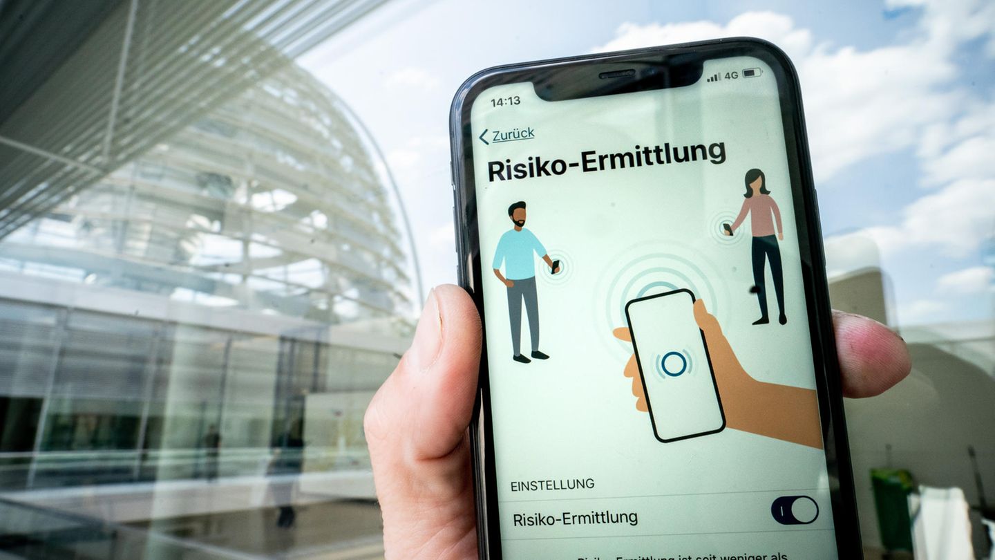 Die Corona-Warn-App mit der Seite zur Risiko-Ermittlung ist im Display eines Smartphone vor der Kuppel des Reichstags zu sehen