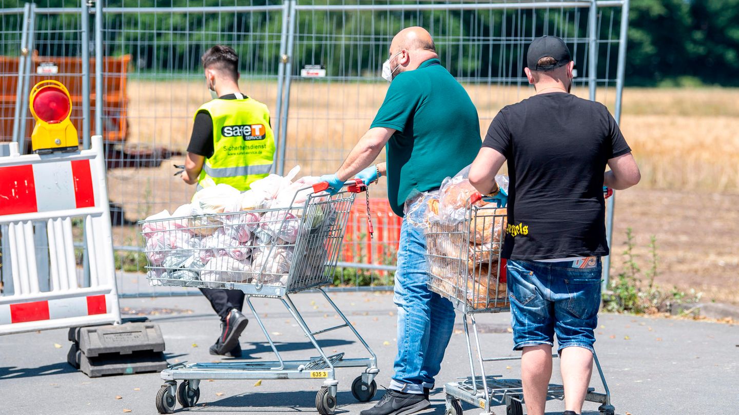 Tönnies: Zwei Mitarbeiter eines Lebensmittelmarktes schieben in zwei Einkaufswagen Brot in die abgesperrte Siedlung