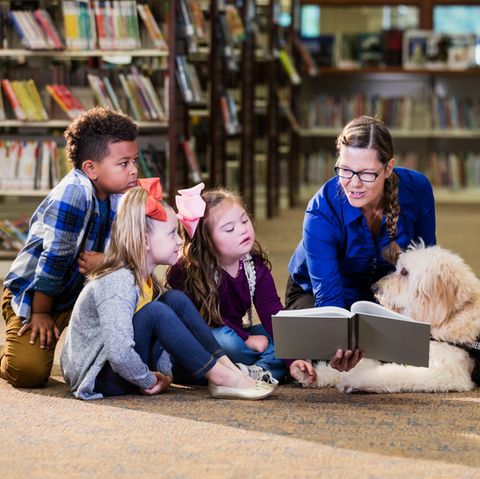 Kinder, eine Lehrerin und ein Hund sitzen um ein Buch