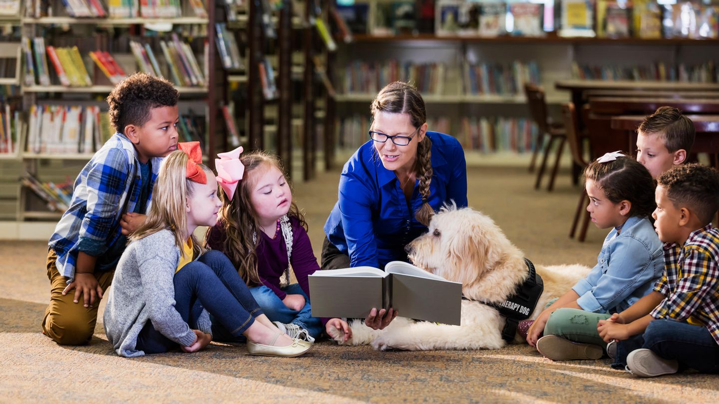 Kinder, eine Lehrerin und ein Hund sitzen um ein Buch
