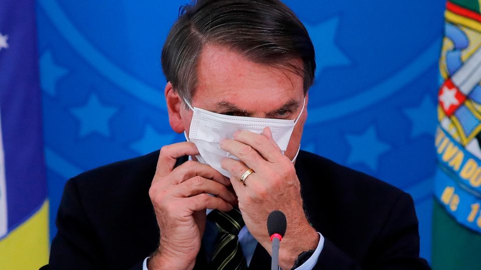 Bolsonaro versucht eine Maske aufzusetzen