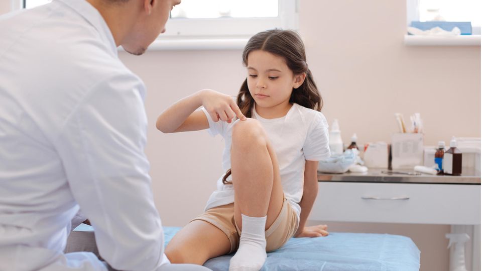 Rheuma bei Kindern: Ein Mädchen teilt dem Arzt Schmerzen im Knie mit
