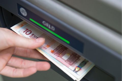 Eine linke Hand greift nach einem Euro-Scheinen, die aus dem Schacht eines Geldautomaten ragen