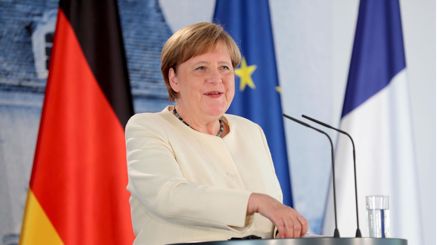 Angela Merkel steht an einem Rednerpult und lächelt