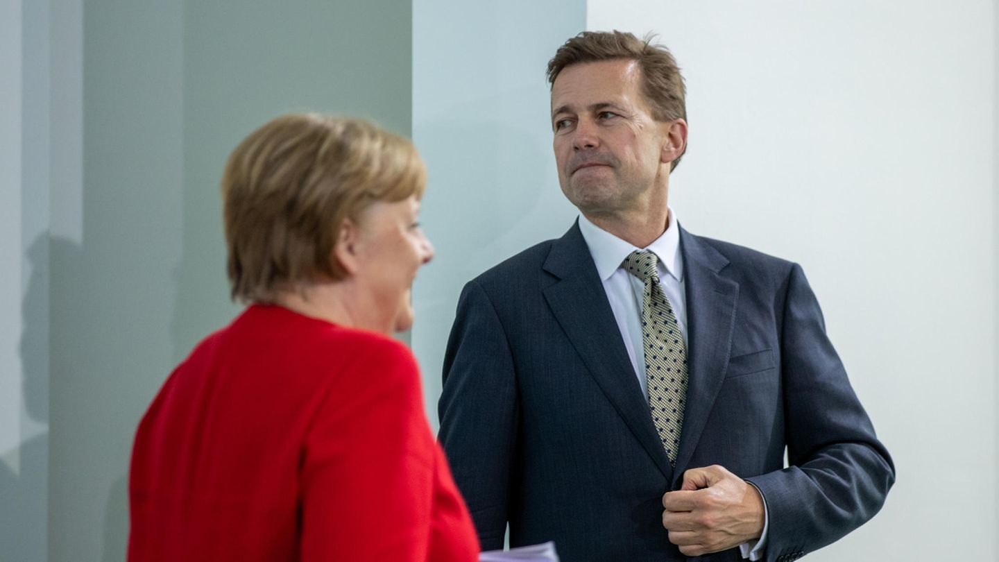 Angela Merkel geht in rotem Blazer an Pressesprecher Seibert in Anzug und Krawatte vorbei