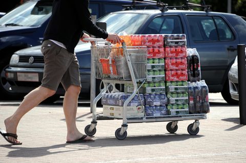 Ein Einkaufswagen voller Getränkedosen wird über den Parkplatz geschoben