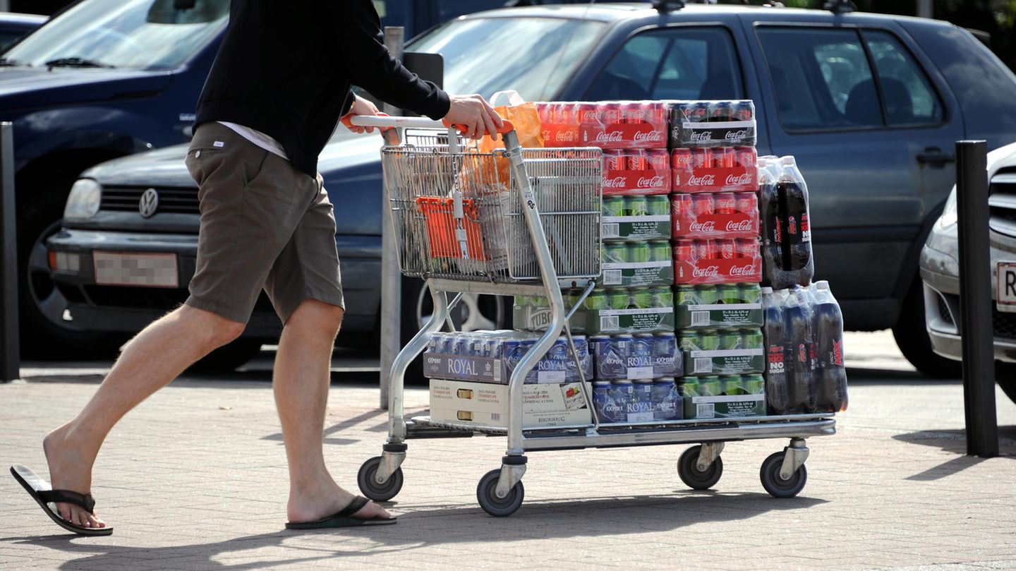 Ein Einkaufswagen voller Getränkedosen wird über den Parkplatz geschoben