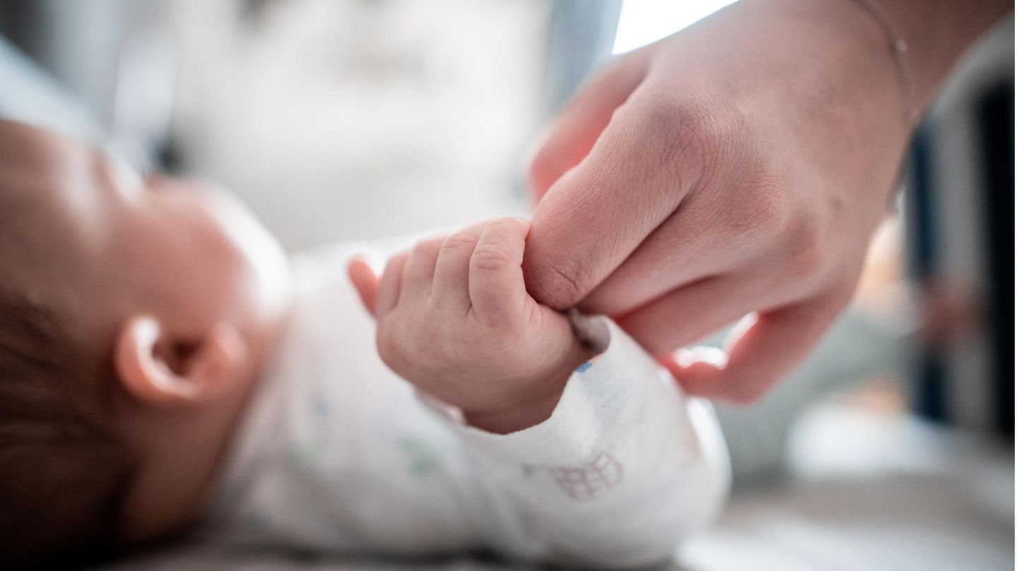Ein Baby klammert sich an den Finger seiner Mutter