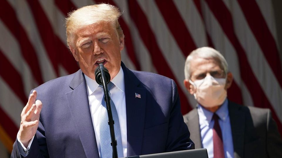 US-Präsident Donald Trump bei einer Rede, hinter ihm steht sein maskierter Gesundheitsexperte Anthony Fauci US-Präsident Donald Trump bei einer Rede, hinter ihm steht sein maskierter Gesundheitsexperte Anthony Fauci