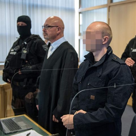 Der Angeklagte im Halle-Prozess im Gerichtssaal mit Anwalt und zwei Polizisten