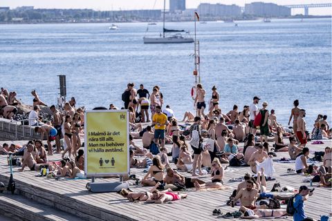 In Malmö genießen Menschen das warme Wetter am Wasser. Ein Schild weißt auf Abstandsregeln hin. 