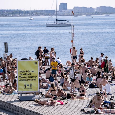 In Malmö genießen Menschen das warme Wetter am Wasser. Ein Schild weißt auf Abstandsregeln hin. 