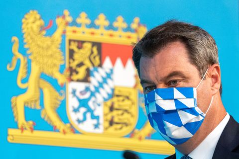 Bayerns Ministerpräsident Markus Söder mit weiß-blauer Gesichtsmaske vor bayerischem Wappen